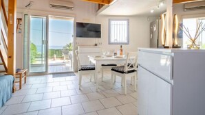 A modern kitchen with white cabinets, a dining area with a table and chairs, and a view of the outdoors through a sliding glass door.