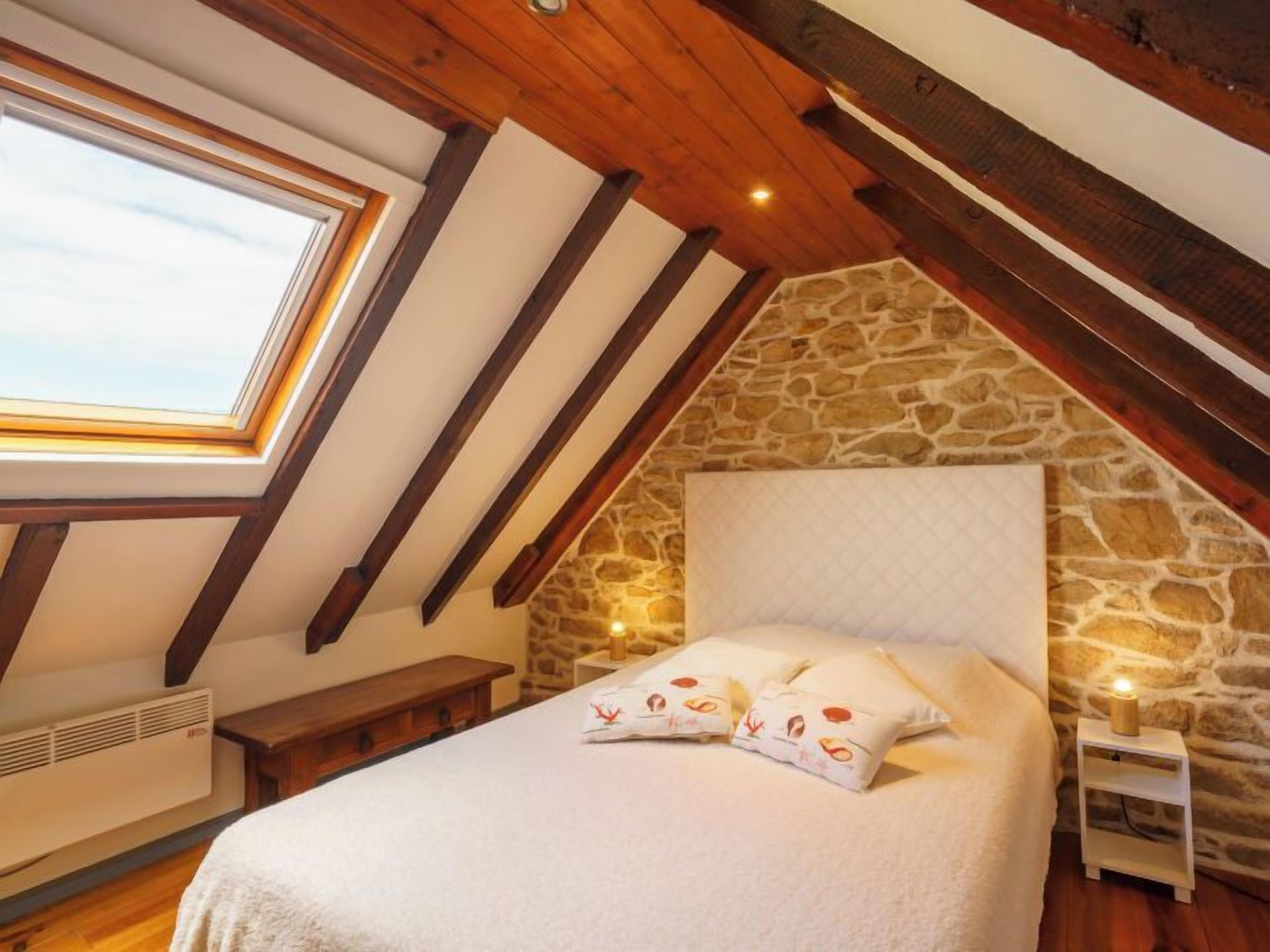 Ein Schlafzimmer mit Steinsandsteinwand, Holzboden, einem Oberlicht, einem Bett mit Kissen und einem Nachttisch mit Lampe.