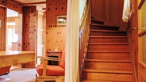 Un interior de madera con una escalera, una silla y una mesita.