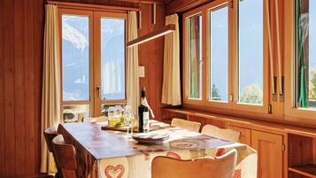 Une salle à manger en bois avec une table dressée pour quatre personnes, de grandes fenêtres et une bouteille de vin posée sur la table.