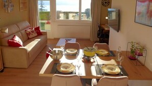 Un salon avec un canapé, une table à manger dressée pour quatre personnes et un téléviseur fixé au mur.