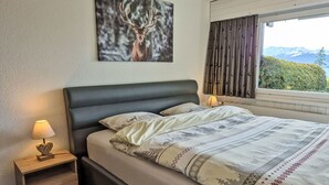 Une chambre à coucher avec un lit, une table de chevet avec une lampe, un tableau représentant un cerf accroché au mur, et une fenêtre avec des rideaux.