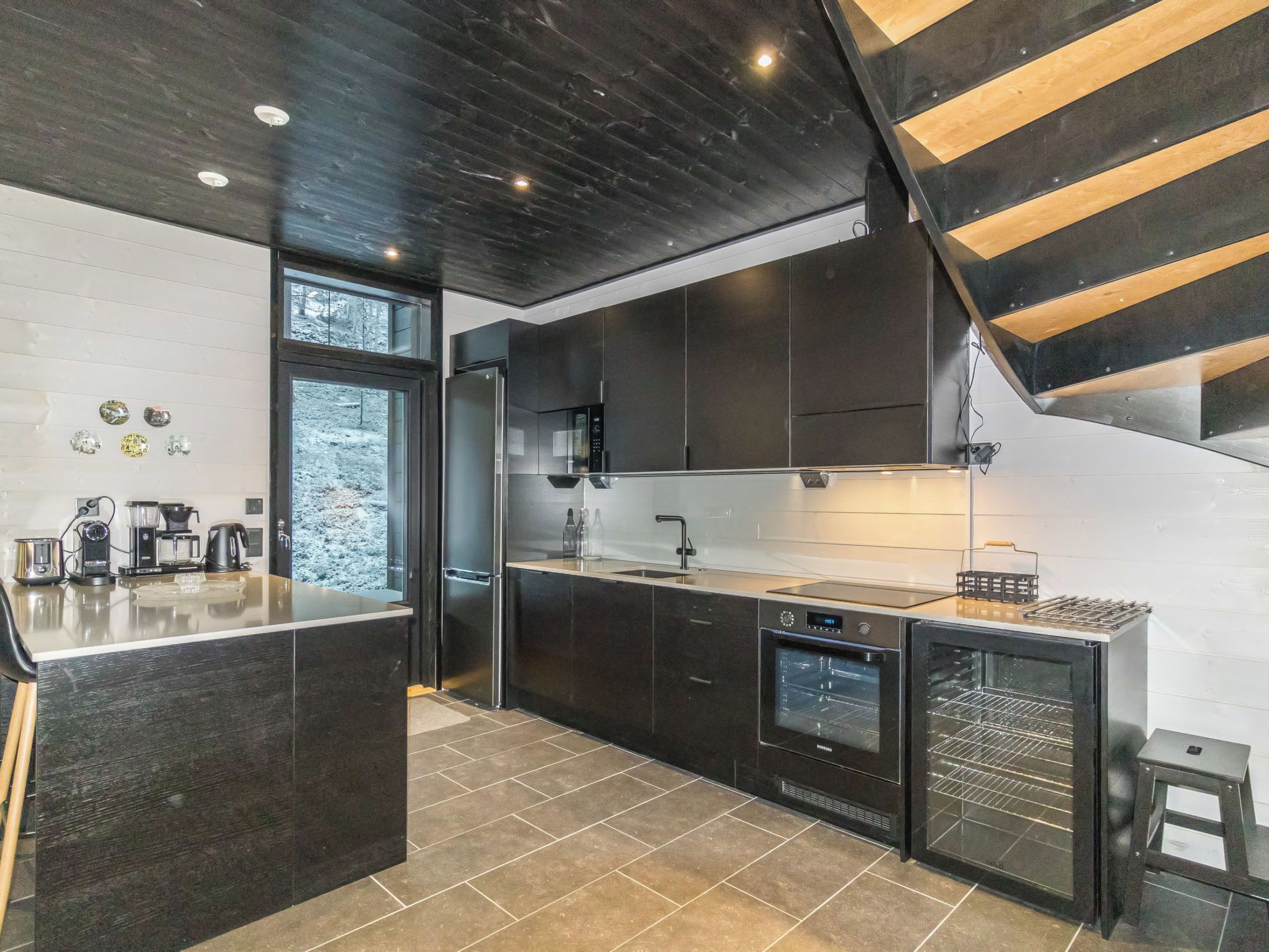 A modern kitchen with a central island, built-in appliances, and a wooden staircase.
