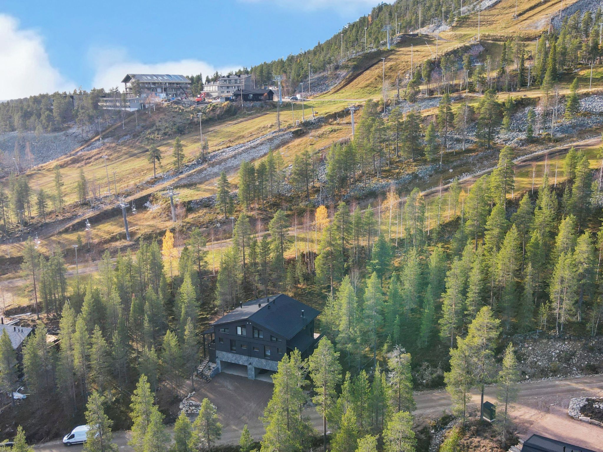 A modern house with a dark roof, surrounded by a forested hillside.