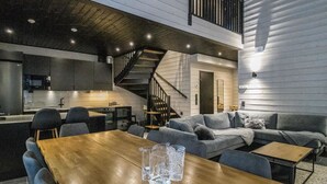 Een modern interieur met een houten eettafel, grijze banken, een trap en een keuken.