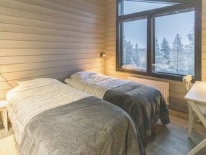 Une chambre avec deux lits, une fenêtre donnant sur des arbres et une table blanche.