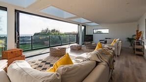 Ein geräumiges Wohnzimmer mit einem großen Glasfenster, das auf einen Balkon führt, einer Sofagarnitur, einem Fernseher und einem Holzboden.
