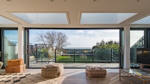 Ein modernes Wohnzimmer mit großen Fenstern, einem Flachbildfernseher und Blick auf Garten und Stadtlandschaft.