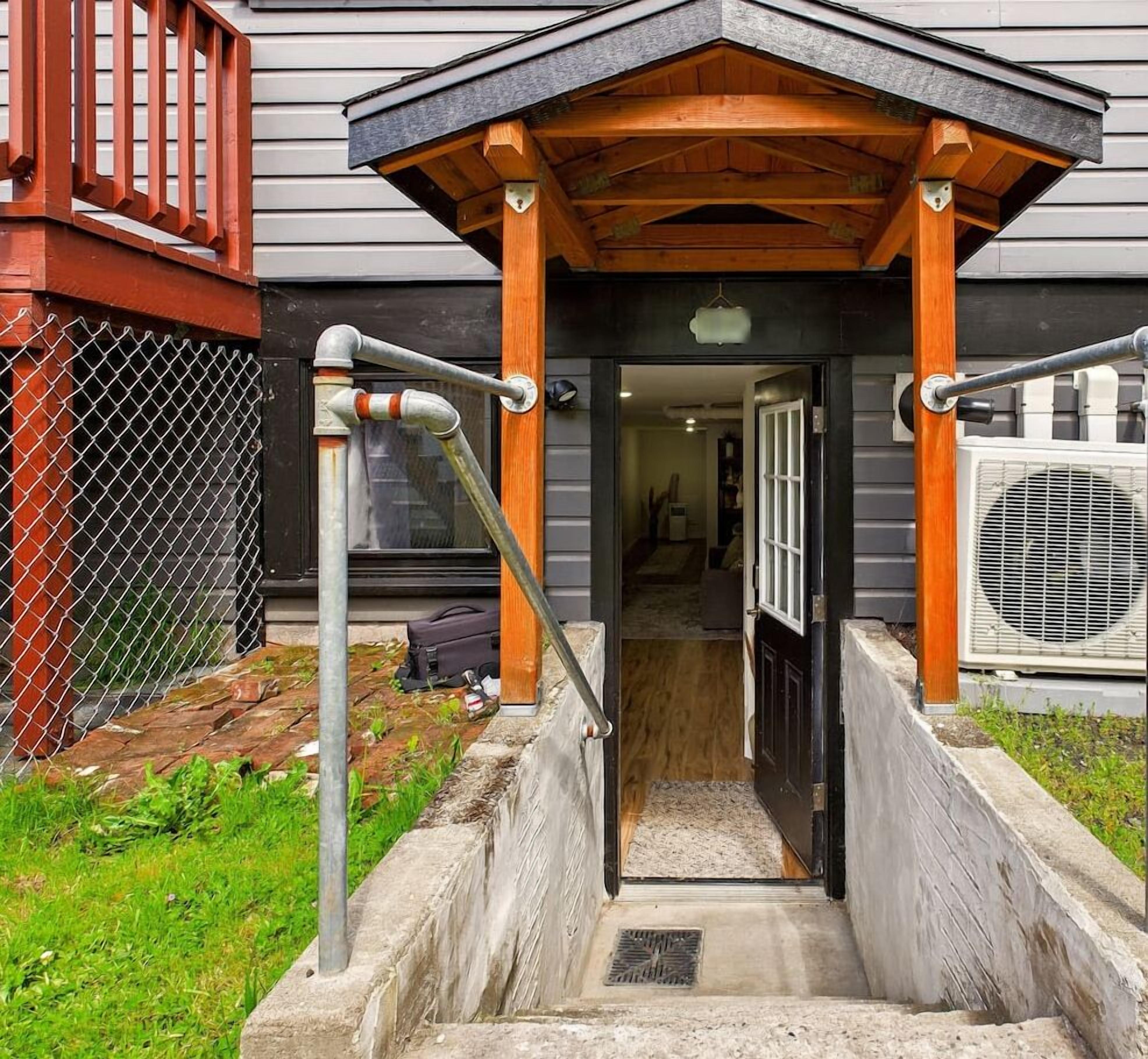 A covered entrance with a wooden porch, a metal gate, and an air conditioning unit.