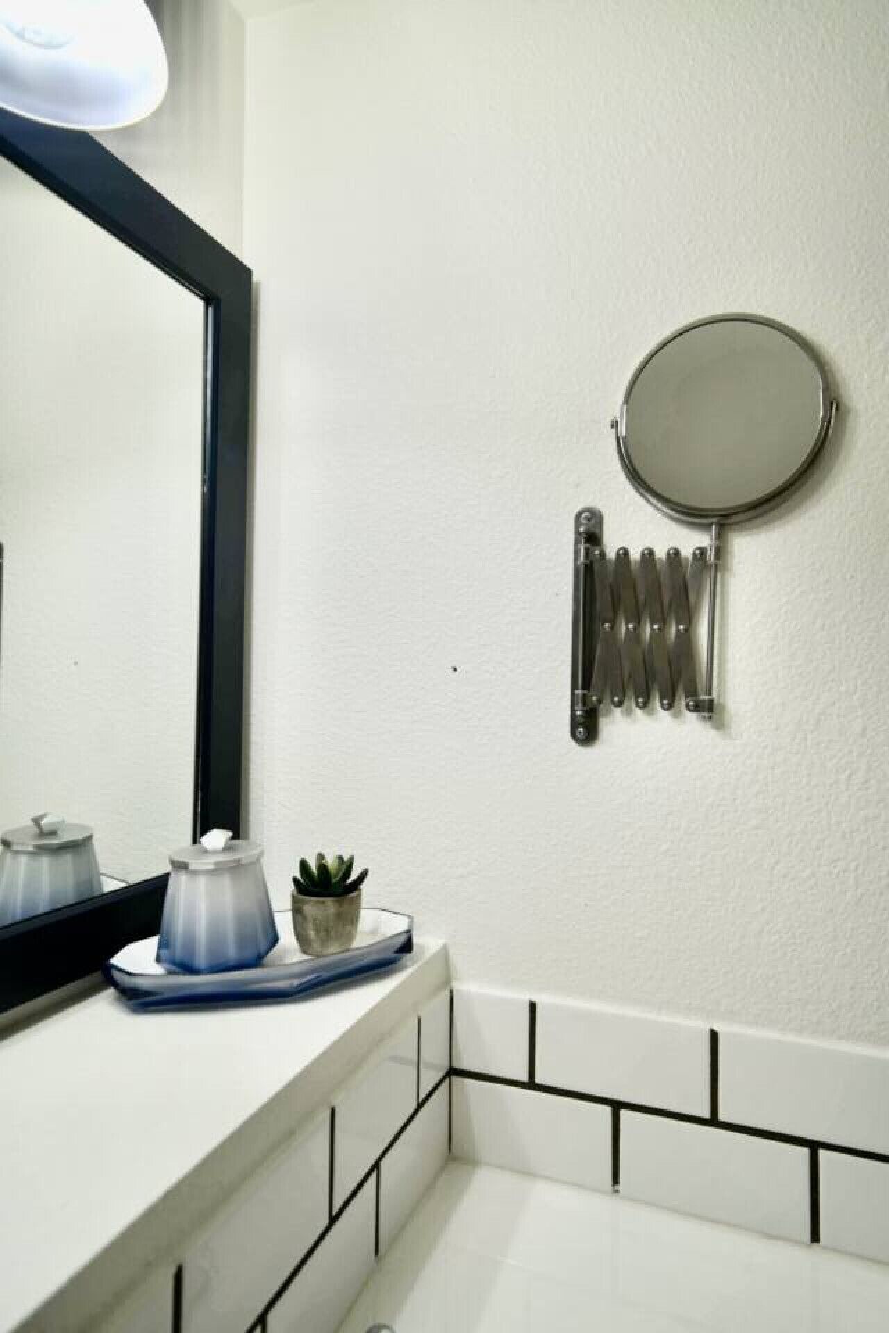 Un baño con un lavamanos blanco, un espejo, un espejo redondo y un toallero.