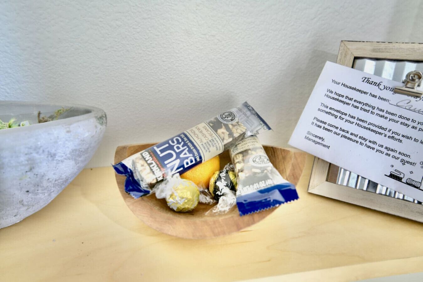Een houten dienblad met een chocoladereep, een ingepakt snoepje en een kleine schaal eten. Een bedankbriefje zit aan het dienblad geknipt.