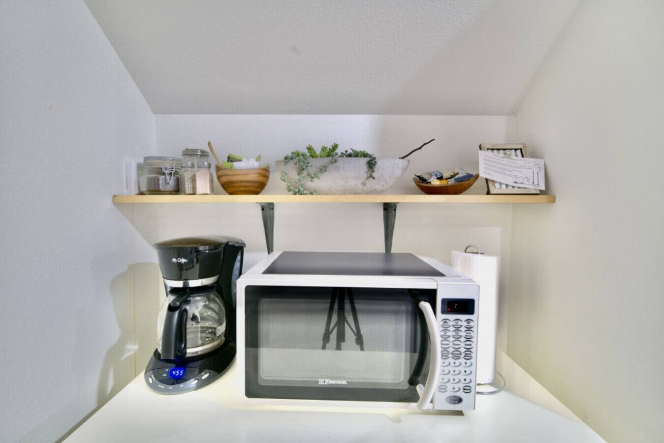 Una cocina con microondas, cafetera y estantes con utensilios de cocina.