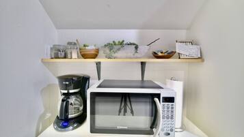 Una cocina con microondas, cafetera y estantes con utensilios de cocina.