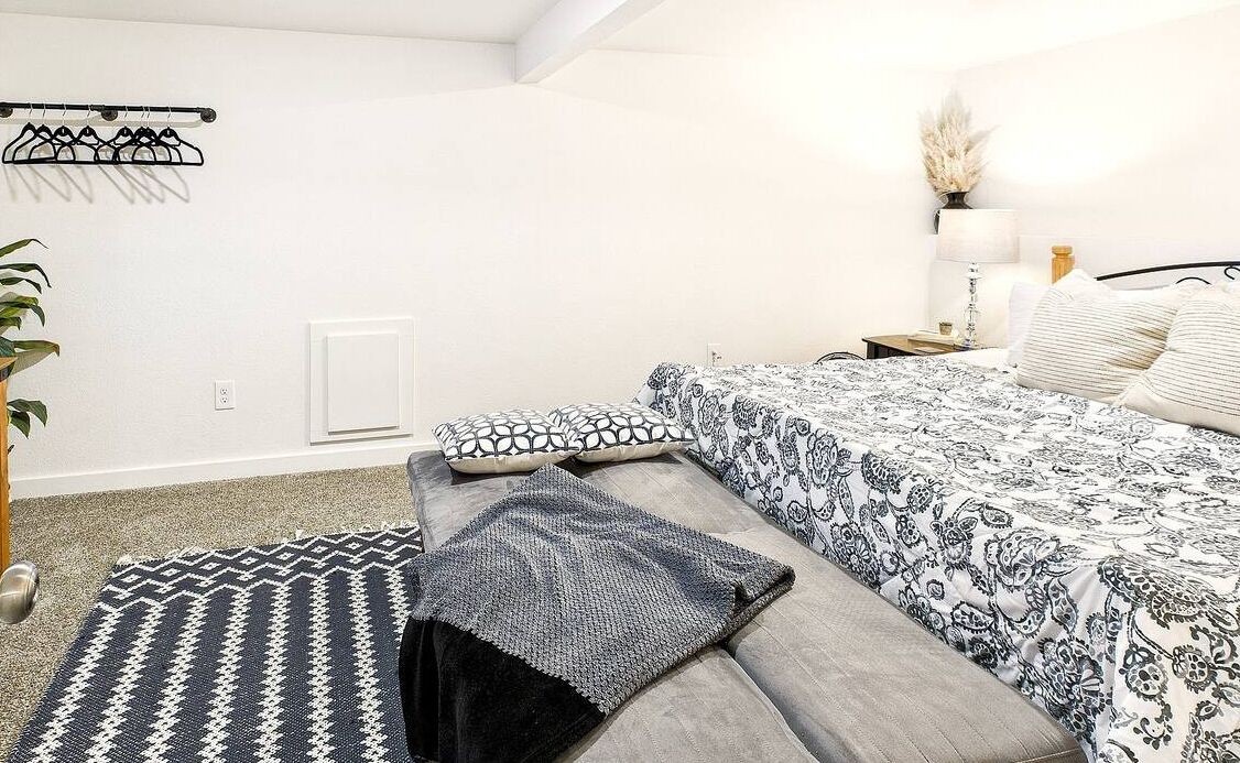A bedroom with a bed, a bedside table with a lamp, a hanging clothes rack, and a patterned rug.