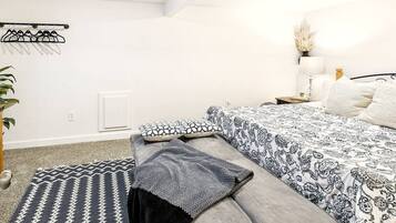 A bedroom with a bed, a bedside table with a lamp, a hanging clothes rack, and a patterned rug.