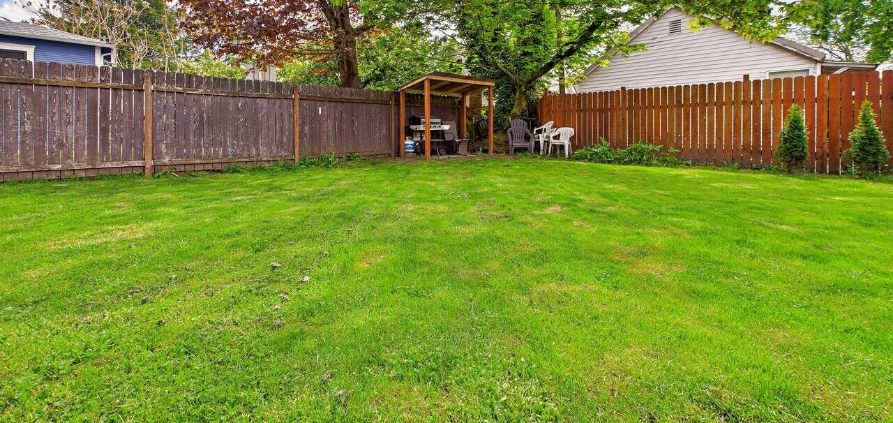 Ein Garten mit Holzzaun, einer überdachten Terrasse und einem Rasen.