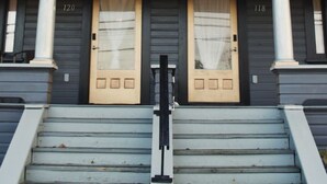 Un edificio a due piani con facciata simmetrica, dotato di due porte con tende, una scala centrale e un piccolo balcone.