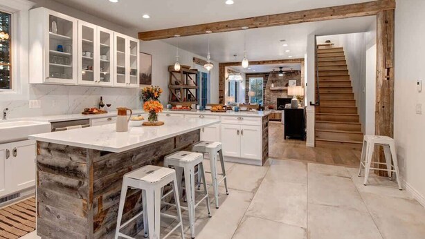A modern kitchen with white cabinetry, a central island with stools, and a rustic wooden accent. - Abode at Palomino Ridge, amazing views, nature (Jackson)