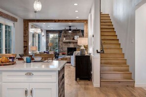A kitchen with a wooden staircase, a stone fireplace, and a dining area with a view of the outdoors.