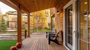 A wooden deck with chairs and a covered area, a glass door, and a view of a forested area. - Abode at Palomino Ridge, amazing views, nature (Jackson)