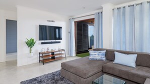 A modern living room with a brown sofa, a glass coffee table, a flat-screen TV mounted on the wall, and a sliding glass door leading to a balcony. - San Lameer Villa Rentals 2818 (Southbroom)