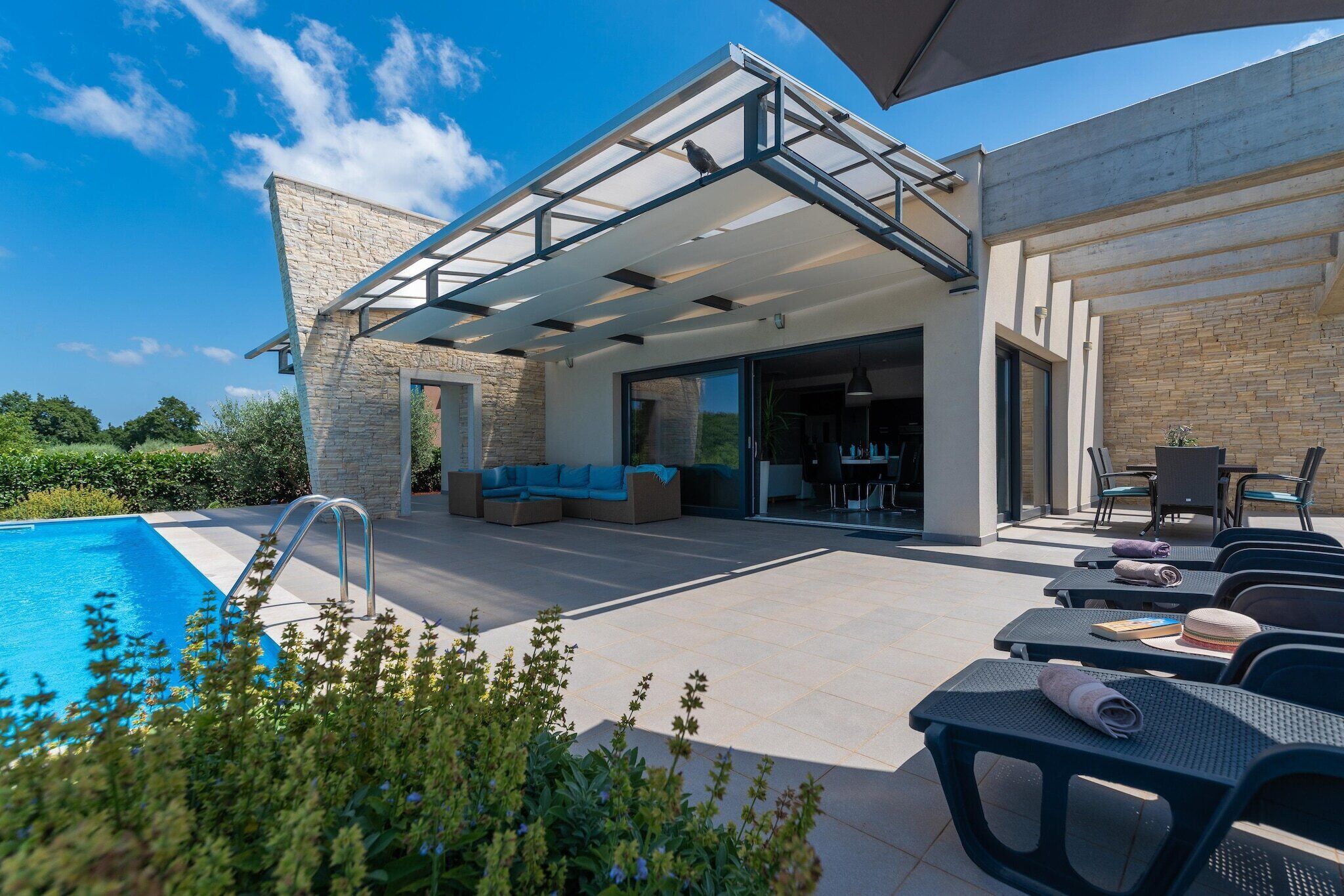 A modern outdoor patio with a pool, seating area, and a covered section with tables and chairs.