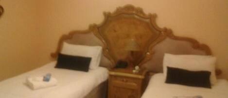 Una habitación con dos camas individuales, cada una con una almohada y una mesita con lámpara.