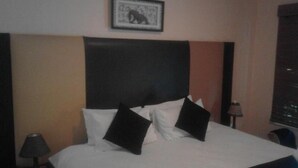 A hotel room with a large bed, black and white pillows, a framed picture on the wall, and a lamp on a side table. - dejazzy guest house (Johannesburg)