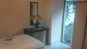 A hotel room with a bed, a desk, a chair, a vase with flowers, and a mirror on the wall. - dejazzy guest house (Johannesburg)