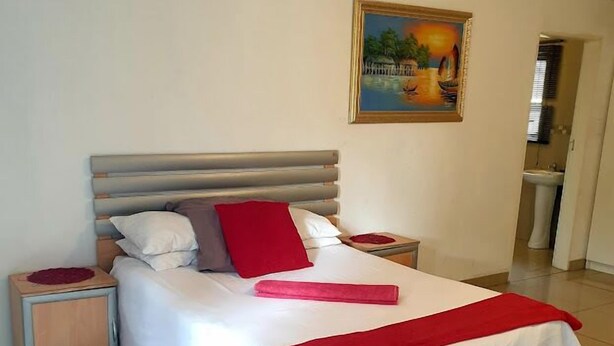 A neatly made bed with a white and red bedspread, two nightstands with red and white lamps, a painting on the wall, and a leopard print rug on the floor. - dejazzy guest house (Johannesburg)