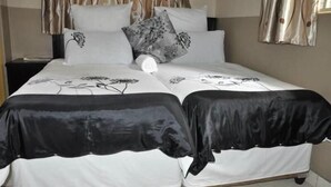 A double bed with a floral bedspread, two pillows with a floral pattern, and a bedside table with a lamp. - dejazzy guest house (Johannesburg)