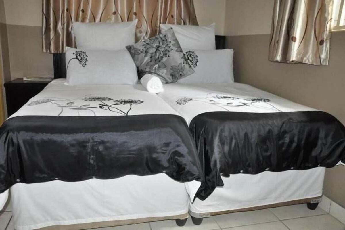 Ein Doppelbett mit blumigem Bettbezug, zwei Kissen mit floralem Muster und ein Nachttisch mit Lampe.