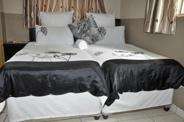 Ein Doppelbett mit blumigem Bettbezug, zwei Kissen mit floralem Muster und ein Nachttisch mit Lampe.