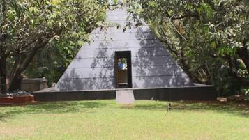 A grassy area with a triangular structure featuring a door, surrounded by trees.