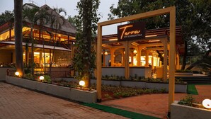 A restaurant named "Terra by Sorrentina" with an outdoor seating area, illuminated by ambient lighting, and surrounded by greenery. - Outpost (Alibag)