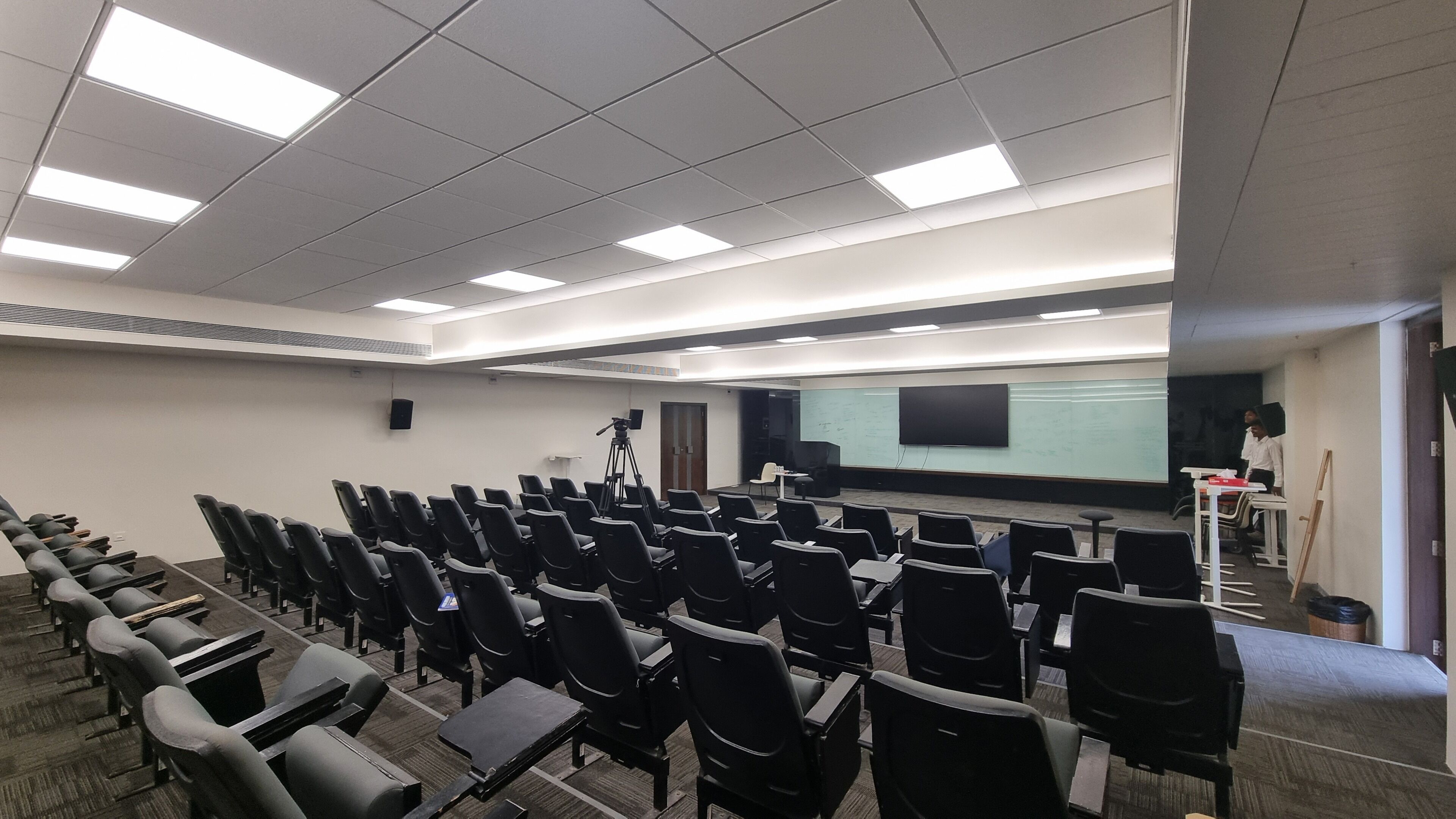 A conference room with rows of chairs, a projector screen, and a whiteboard.