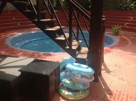 Zona de piscina con un jacuzzi circular, escalones de madera y flotadores inflables.
