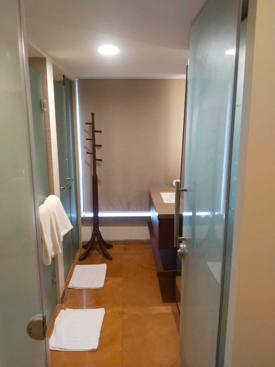 Un pasillo estrecho con un perchero de madera, una toalla blanca en la pared y una puerta de cristal que da al baño.