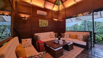 Une pièce chaleureuse avec un plafond en bois, un ensemble de canapés, une table basse et une vue sur la verdure à l’extérieur.