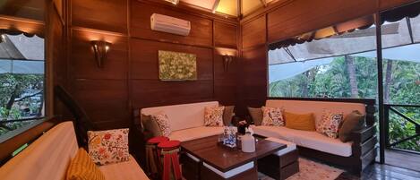A cozy room with a wooden ceiling, a sofa set, a coffee table, and a view of greenery outside.