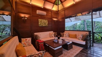 Habitación acogedora con techo de madera, un conjunto de sofás, una mesita de centro y vistas al exterior con vegetación.