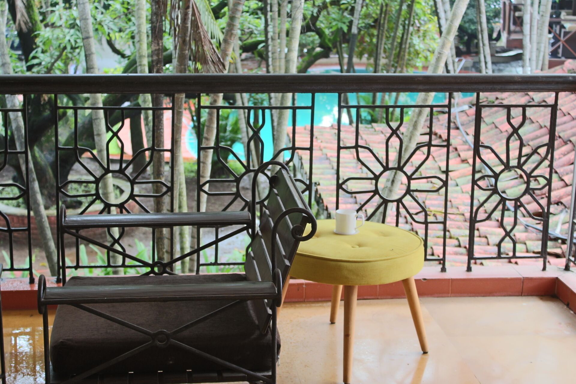 A balcony with a metal railing, a yellow chair, and a small table with a white cup.