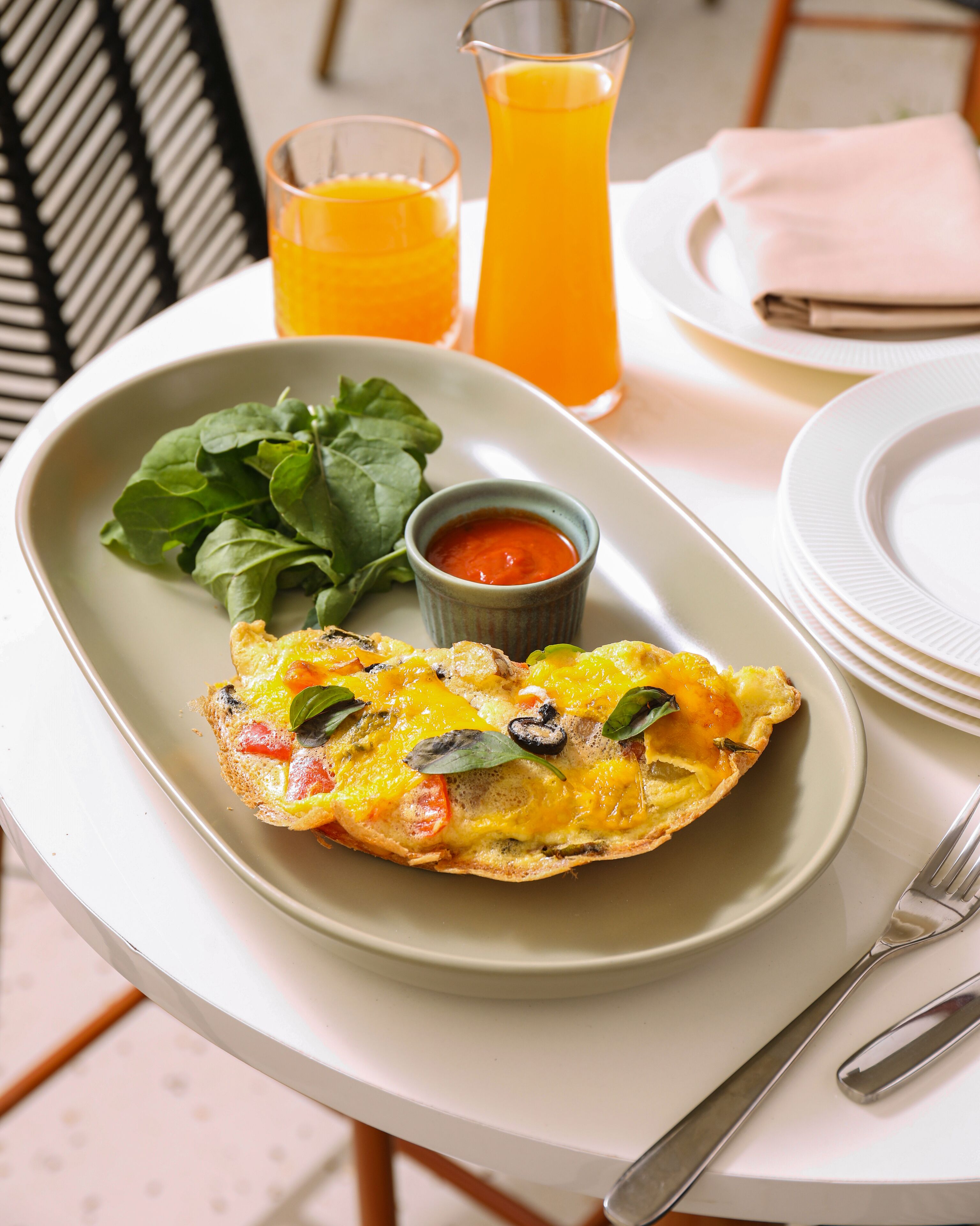 A breakfast plate with a quiche, a glass of orange juice, and a small bowl of sauce on a table with a white tablecloth.