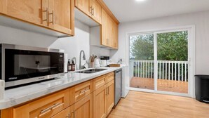 A modern kitchen with wooden cabinets, a built-in microwave, and a large window overlooking a deck. - 1803 Renton · 2b1b Sweet Suite @Renton 10 mins to SeaTac airport (Renton)