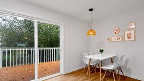 A modern dining area with a white table and chairs, a hanging pendant light, and a view of a wooden deck through large sliding glass doors. - 1803 Renton · 2b1b Sweet Suite @Renton 10 mins to SeaTac airport (Renton)