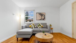 A modern living room with a grey sectional sofa, a round wooden coffee table, and a painting on the wall. - 1803 Renton · 2b1b Sweet Suite @Renton 10 mins to SeaTac airport (Renton)