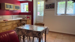 A kitchen with wooden cabinets, a red wall, a dining table with chairs, and a window with a view of a field. - Views of Sault, cycling, hiking, Mont Ventoux (Sault)