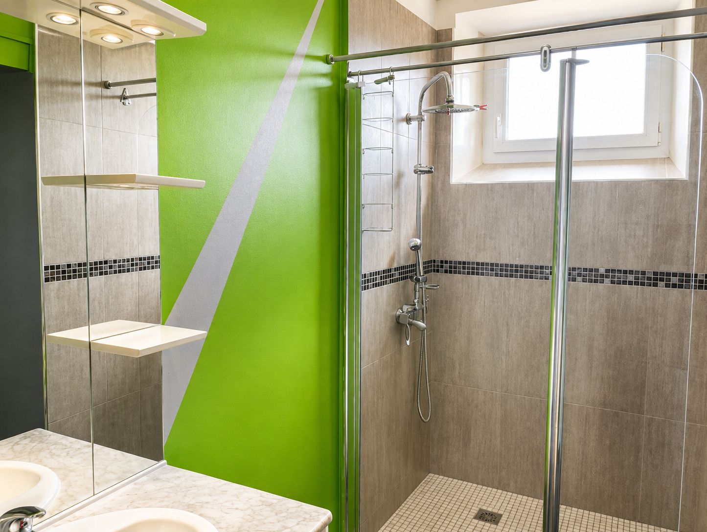 Un baño moderno con cabina de ducha de vidrio, lavamanos blanco y una pared de acento verde.
