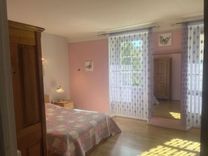 A bedroom with a bed, a nightstand, a lamp, a mirror, and a window with curtains.