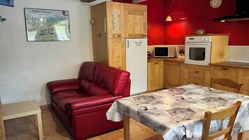 Eine kompakte Küche mit Holzausstattung, einem roten Sofa, einem Esstisch mit Tischdecke in Zeitungsoptik und einer Wandkarte.